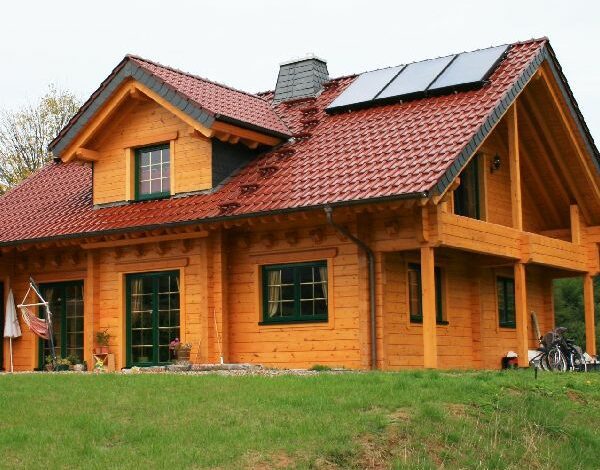 Außenansicht eines FINNHOLZ Blockbohlenhauses mit Solarkollektoren auf dem Dach und traditionellem Holzdesign.