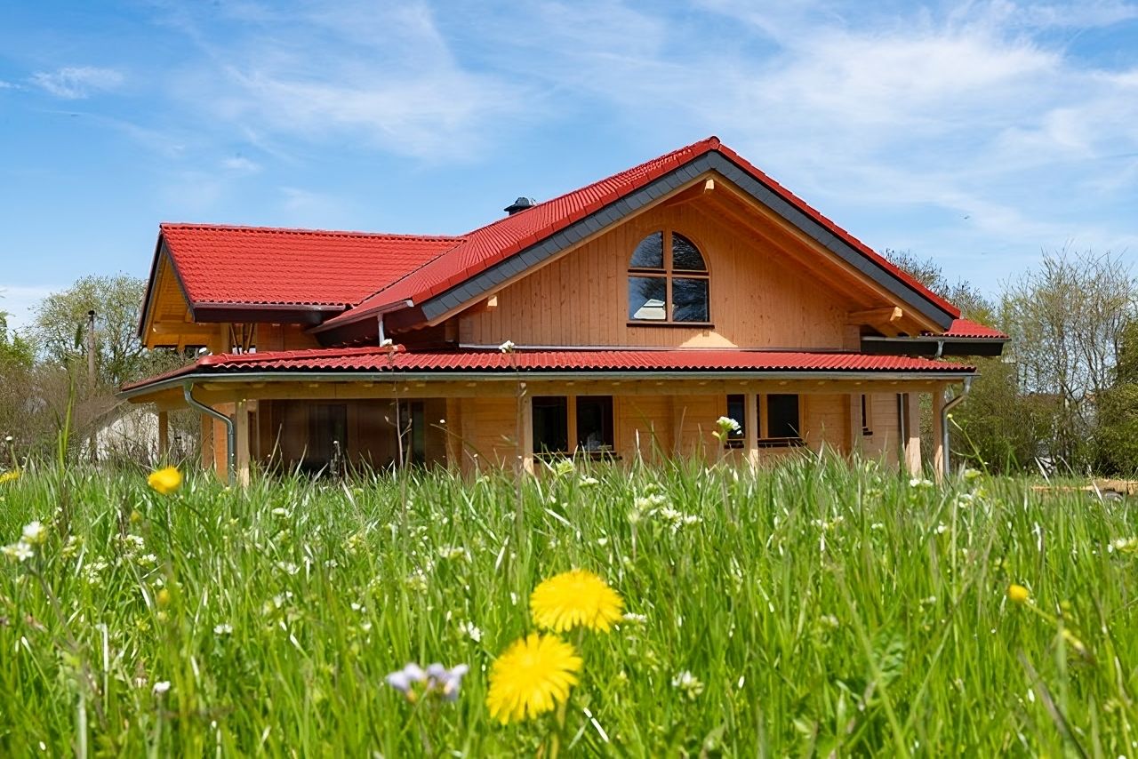 Blockbohlenhaus von FINNHOLZ inmitten einer grünen Wiese mit rotem Dach und natürlichem Holzfinish.