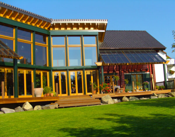 Modernes FINNHOLZ Blockbohlenhaus mit großzügigen Fensterfronten und natürlicher Holzstruktur in idyllischer Lage.