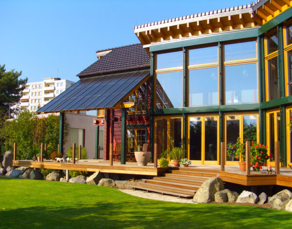 Modernes FINNHOLZ Blockbohlenhaus mit großen Fensterfronten und Solaranlage im grünen Garten.