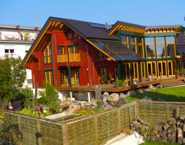 FINNHOLZ Blockhaus mit roter Holzfassade und großer Glasfront in einem liebevoll gestalteten Garten.