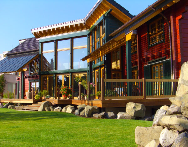 Ein modernes FINNHOLZ Blockbohlenhaus mit großer Glasfront und Holzterrasse umgeben von einem gepflegten Rasen und Steindekor.