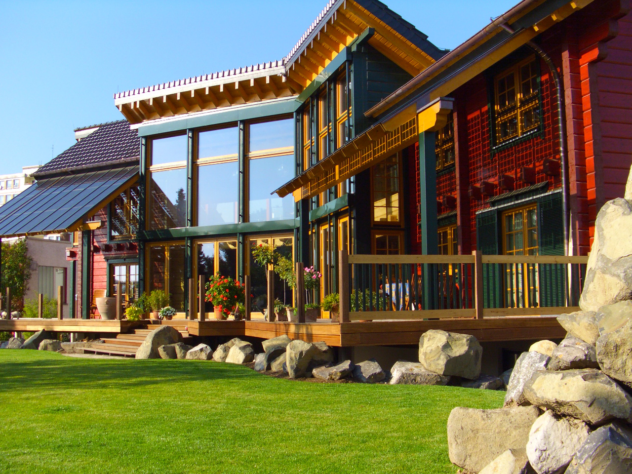 Ein modernes FINNHOLZ Blockbohlenhaus mit großer Glasfront und Holzterrasse umgeben von einem gepflegten Rasen und Steindekor.