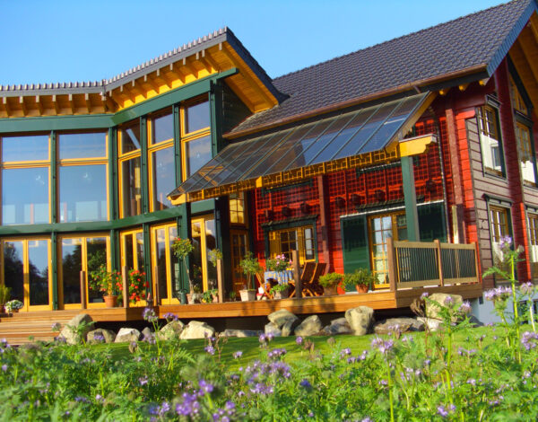 Eindrucksvolles FINNHOLZ Blockhaus mit einer Kombination aus Glas und rotbraunen Holzelementen, integriert in eine natürliche Gartenlandschaft.