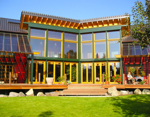 Modernes FINNHOLZ Blockbohlenhaus mit beeindruckender Glasfassade und sonniger Terrasse, umgeben von einem grünen Garten.