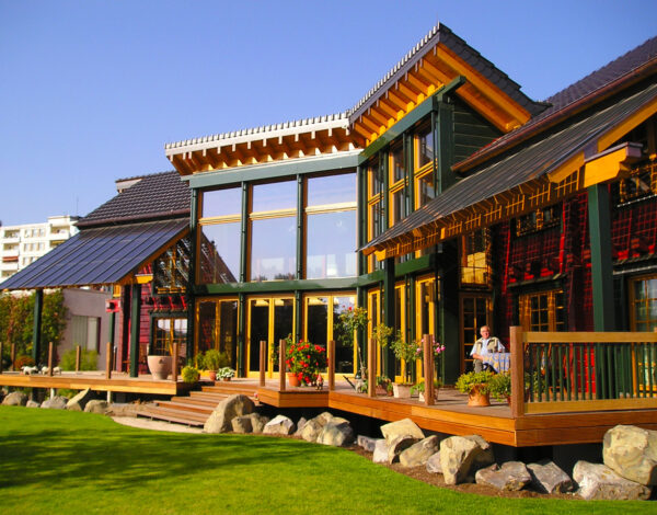Großzügiges FINNHOLZ Blockbohlenhaus mit moderner Glasfassade und sonniger Terrasse, eingebettet in eine idyllische Gartenlandschaft.