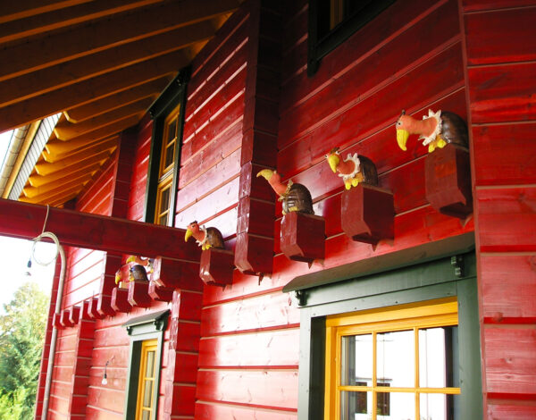 Detailansicht der rot gestrichenen Holzfassade eines FINNHOLZ Blockbohlenhauses mit dekorativen Vogelhäuschen.