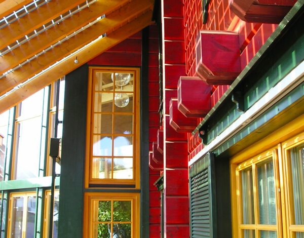 Nahaufnahme einer roten Holzfassade mit kunstvollen Schnitzereien eines FINNHOLZ Blockbohlenhauses, das Handwerk und Design kunstvoll vereint.