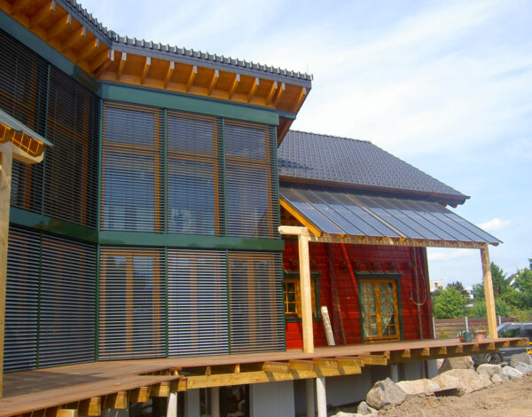 Ansicht eines FINNHOLZ Blockbohlenhauses in der Bauphase mit einer Kombination aus roter Holzverkleidung und großen Fensterfronten.
