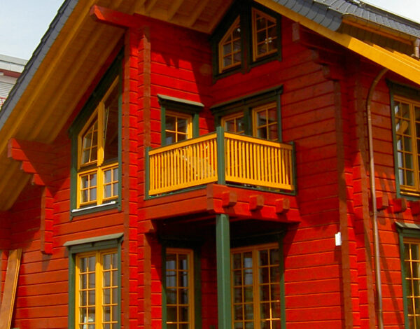 Traditionelles rotes FINNHOLZ Blockhaus mit Balkon, charakteristisch für hochwertige Holzbauweise.