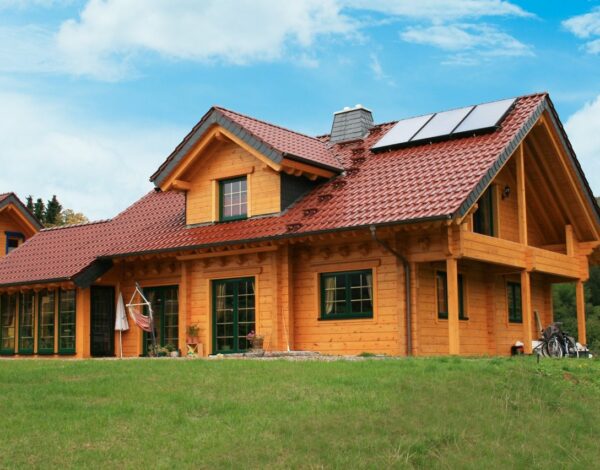 Ländliches FINNHOLZ Blockbohlenhaus mit Solardach und grüner Umgebung.