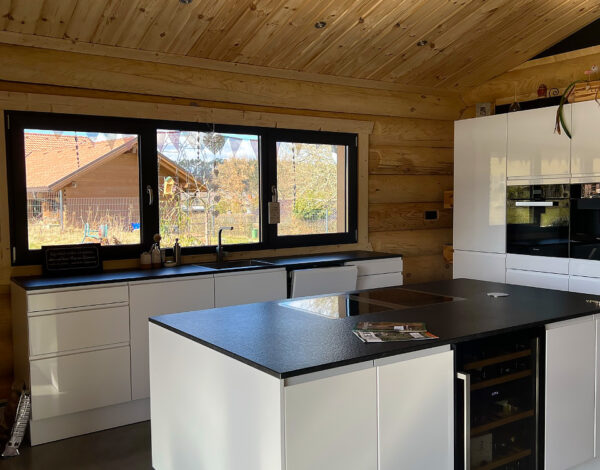 Moderne Küche mit Kochinsel in einem Rundbohlen-Blockhaus von FINNHOLZ, umgeben von natürlichen Holzelementen.