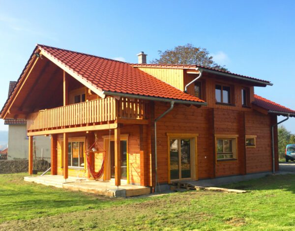 Orangefarbenes Blockbohlenhaus von FINNHOLZ mit Balkon und idyllischem Grün.