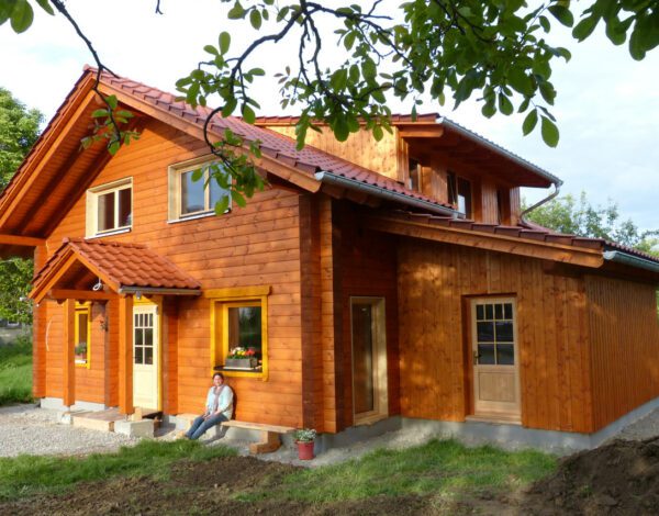 Charaktervolles FINNHOLZ Blockbohlenhaus mit orangener Fassade und natürlicher Umgebung.