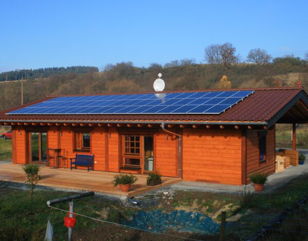 FINNHOLZ Plusenergie-Blockhaus mit Solarpaneelen bei Sonnenschein.