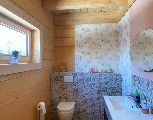 Stilvolles WC im Blockhaus von FINNHOLZ mit Holzvertäfelung und modernen Sanitäranlagen.
