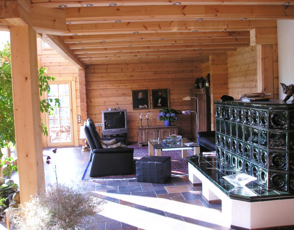 Wohnzimmer im FINNHOLZ Blockbohlenhaus mit traditionellem Ofen und Holzbauweise.