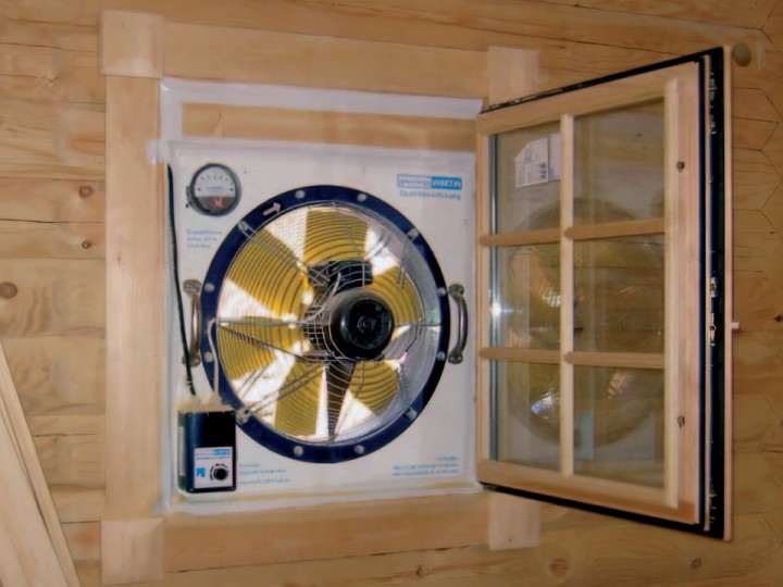Ein Ventilator, der für Blower-Door-Tests verwendet wird, installiert in einem Fensterrahmen eines Blockhauses.