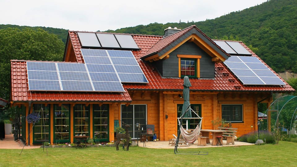 Energieeffizientes Blockbohlenhaus von FINNHOLZ mit Solarpaneelen auf dem Dach und einer gemütlichen Terrasse.
