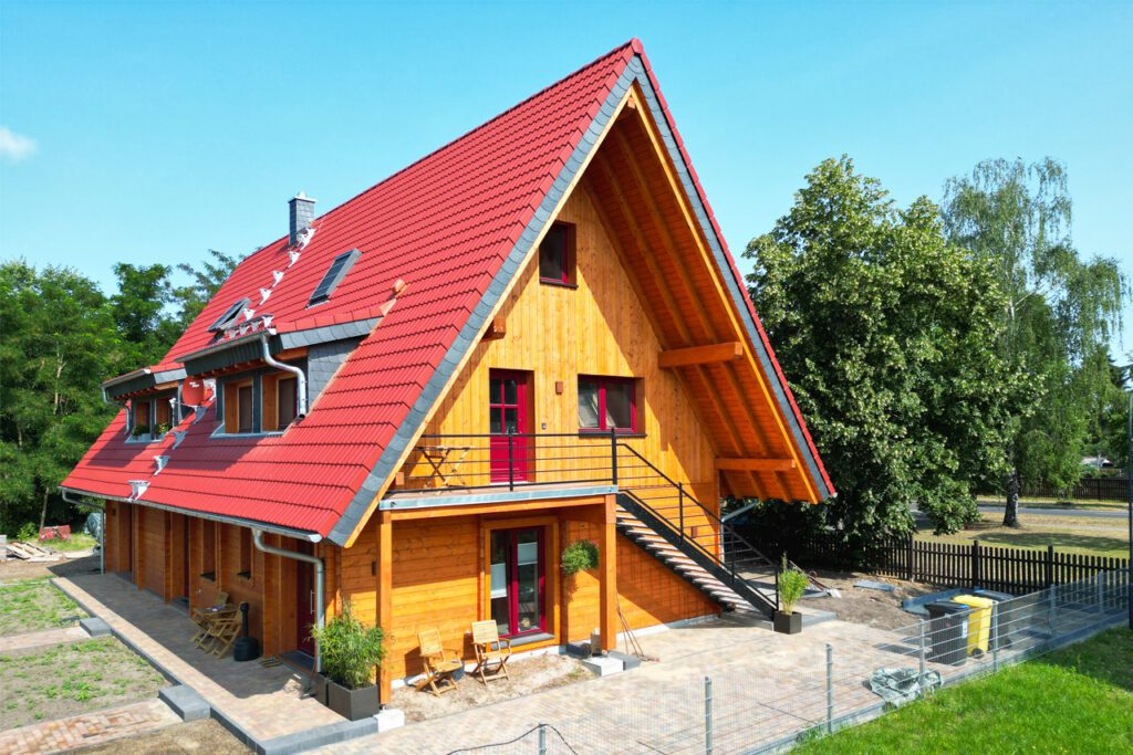 Großzügiges FINNHOLZ Blockhaus mit markantem rotem Dach und natürlicher Holzfassade.
