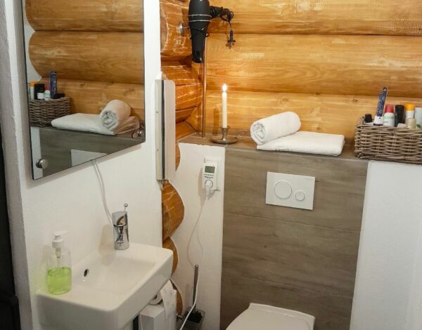 Kompaktes und funktionales Badezimmer im FINNHOLZ Rundbohlenhaus mit natürlicher Holzwand.