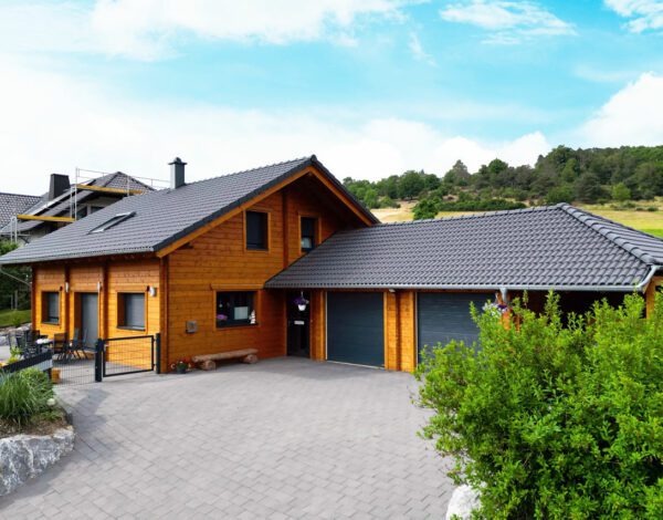 Modernes FINNHOLZ Blockbohlenhaus mit dunklem Dach und Garage.