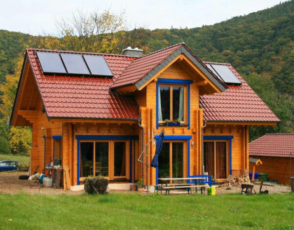 Leuchtendes FINNHOLZ Blockbohlenhaus mit Solardach in herbstlicher Landschaft.