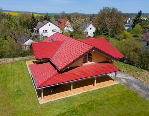 Luftaufnahme eines charmanten FINNHOLZ Blockbohlenhauses mit rotem Dach, umgeben von einer grünen Wiese.