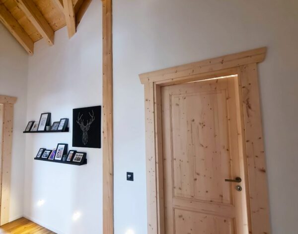 Einladender Flur im Blockbohlenhaus von FINNHOLZ mit natürlichem Holzdekor, einer robusten Holztür und harmonischer Beleuchtung, die die gemütliche Atmosphäre unterstreicht.
