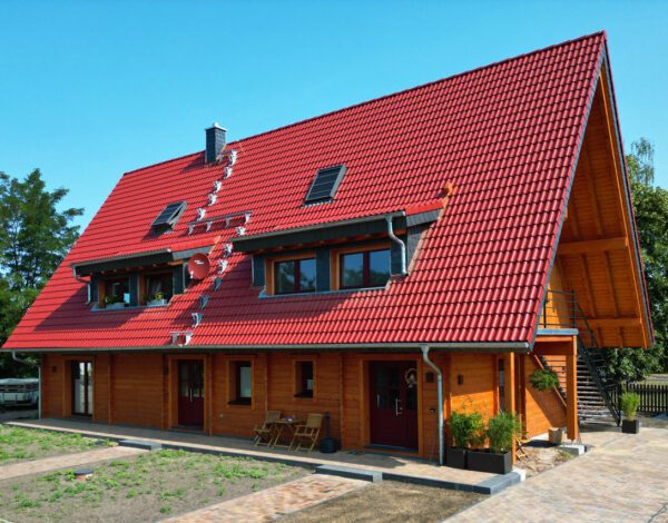 Modernes FINNHOLZ Blockbohlenhaus mit markantem roten Dach und natürlicher Holzfassade aus Blockbohlen.
