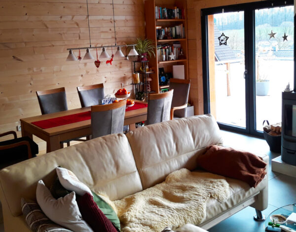 Hell und gemütlich eingerichtetes Wohnzimmer in einem FINNHOLZ Blockbohlenhaus mit Kamin und Blick nach draußen.