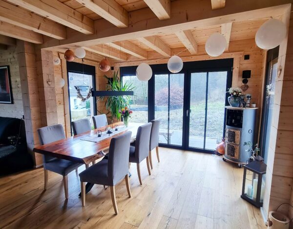 Hell und einladend gestaltetes Wohnzimmer in einem Blockbohlenhaus von FINNHOLZ mit natürlichem Holzinterieur, elegantem Esstisch und modernen Designelementen.