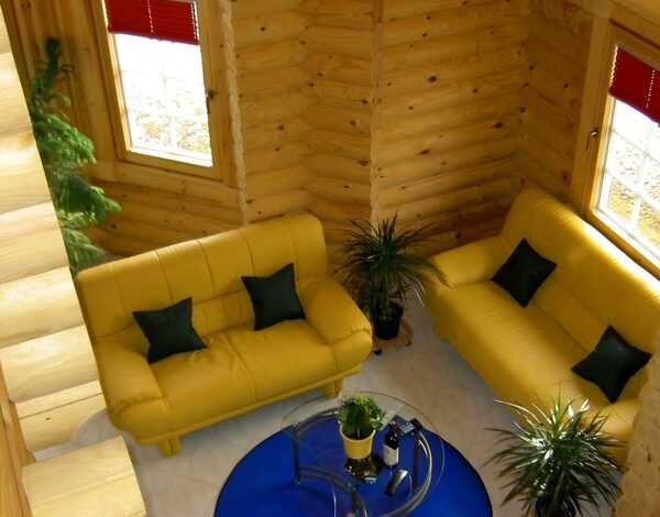 Verschiedene Blickwinkel auf das helle Gästezimmer mit gelben Sofas und Sessel in einem Blockhaus von Finnholz.