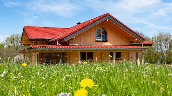 Idyllisches FINNHOLZ Blockhaus mit rotem Dach umgeben von blühender Wiese.