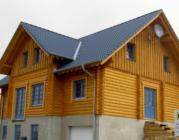 Ansicht eines charmanten FINNHOLZ Blockhauses mit Rundbohlenkonstruktion und blauem Dach.