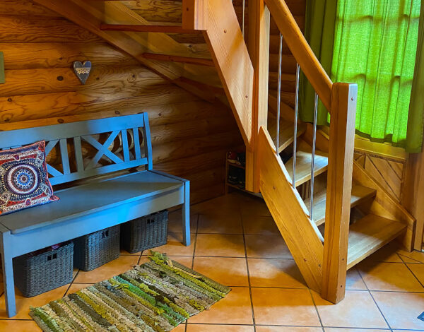 Einladende Diele eines FINNHOLZ Rundbohlen-Blockhauses mit einer handgefertigten Holztreppe und einer gemütlichen Sitzbank.
