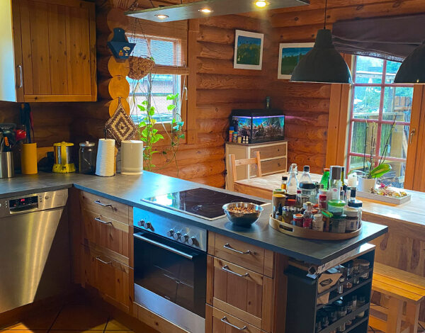 Modern gestaltete Küche in einem Rundbohlen-Blockhaus von FINNHOLZ mit hochwertigen Holzschränken, Edelstahlgeräten und einer gemütlichen Atmosphäre.
