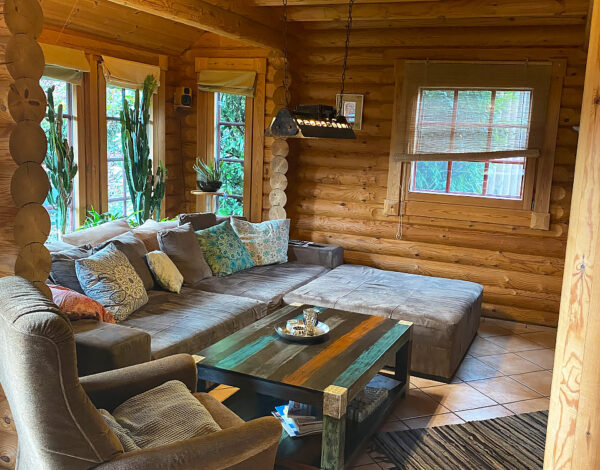Behagliches Wohnzimmer in einem FINNHOLZ Rundbohlen-Blockhaus mit robusten Holzwänden, gemütlichen Sitzgelegenheiten und einem rustikalen Couchtisch.