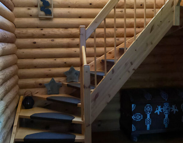 Innenansicht einer Holztreppe in einem FINNHOLZ Rundbohlen-Blockhaus mit natürlichen Holztexturen und handwerklicher Qualität.