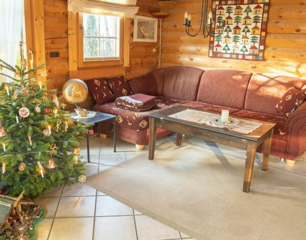 Gemütliches Wohnzimmer in einem Rundbohlen-Blockhaus von FINNHOLZ, geschmückt mit einem festlich dekorierten Weihnachtsbaum.