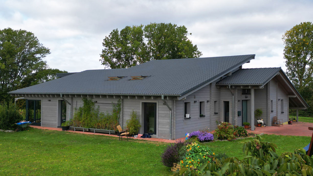 Modernes Holzhaus von FINNHOLZ mit grauem Satteldach und grauer Außenverkleidung, umgeben von einem gepflegten Garten.