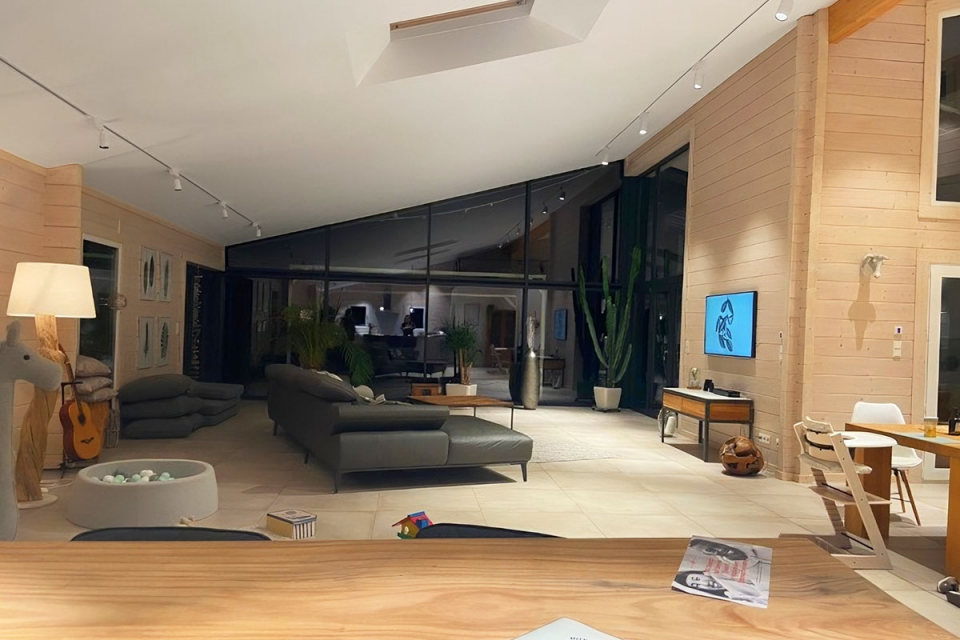 Ein modernes Wohnzimmer in einem FINNHOLZ Wohnblockbohlenhaus mit stilvollem Design, großen Glasfenstern und gemütlicher Atmosphäre.