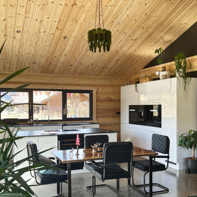 Modern eingerichteter Essbereich im FINNHOLZ Rundbohlen-Blockhaus mit natürlicher Holzdecke und großen Fenstern.