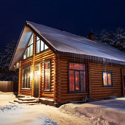 Beleuchtetes FINNHOLZ Rundbohlen-Blockhaus in einer verschneiten Winterlandschaft bei Nacht.