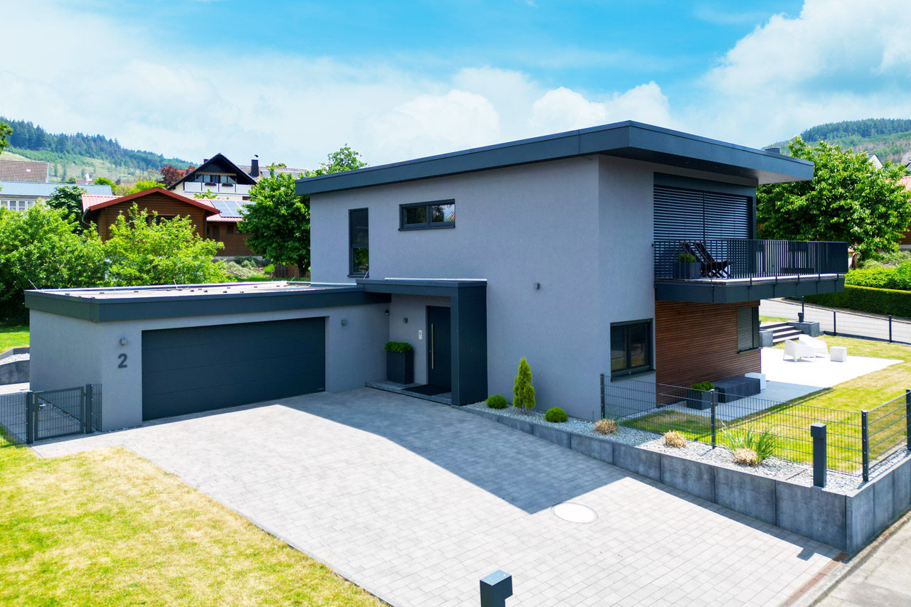 Modernes graues Fertighaus von FINNHOLZ mit großzügiger Einfahrt und grüner Umgebung.