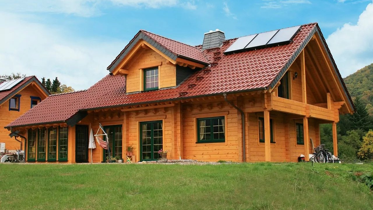 Traditionelles FINNHOLZ Holzhaus mit rotem Dach, erbaut aus Blockbohlen, umgeben von einer natürlichen Landschaft.