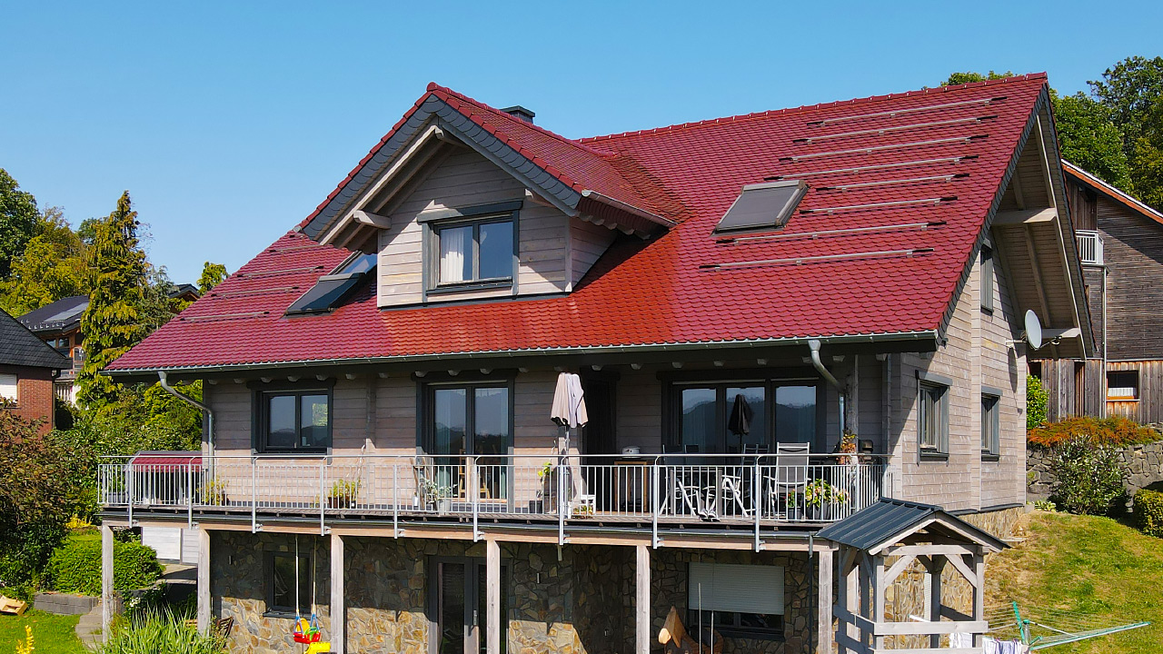 Modernes FINNHOLZ Holzhaus mit rotem Dach und Balkon im Grünen, spiegelt sorgfältige Planung im Holzhaus Preis wider.