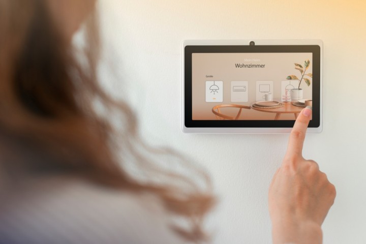 Eine Frau bedient ein Smart-Home-System auf einem Wandbildschirm, um verschiedene Geräte im Wohnzimmer zu steuern.