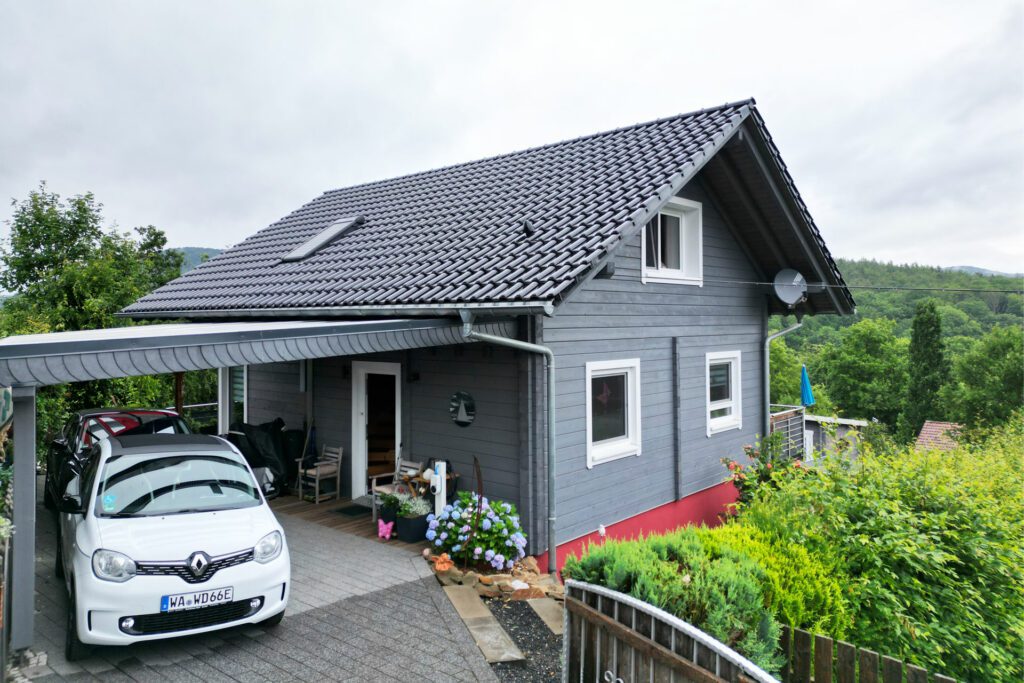 Schönes FINNHOLZ Ferienhaus mit grauen Wänden und Dach, umgeben von lebhaftem Grün.