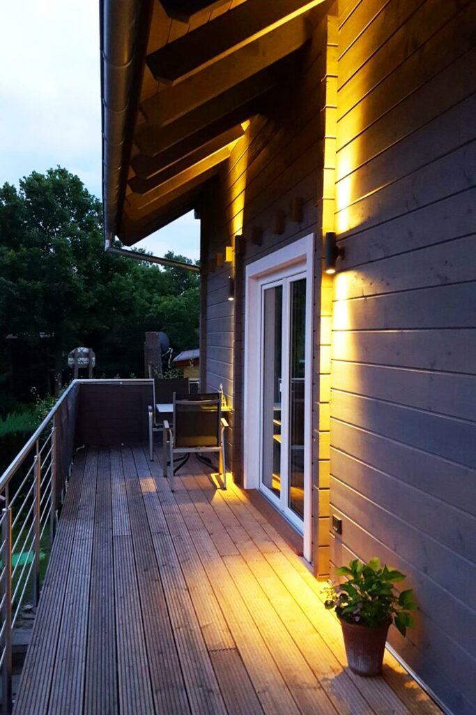 Abendansicht eines FINNHOLZ Ferienhauses mit beleuchtetem Holzfassade und Holzboden des umlaufenden Balkons.